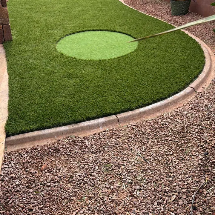 Turf lawn with a small putting cup, finished with a concrete mow curb against red lava rock